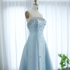 Light blue evening gown with crystal embellishments on a mannequin against a white curtain background.