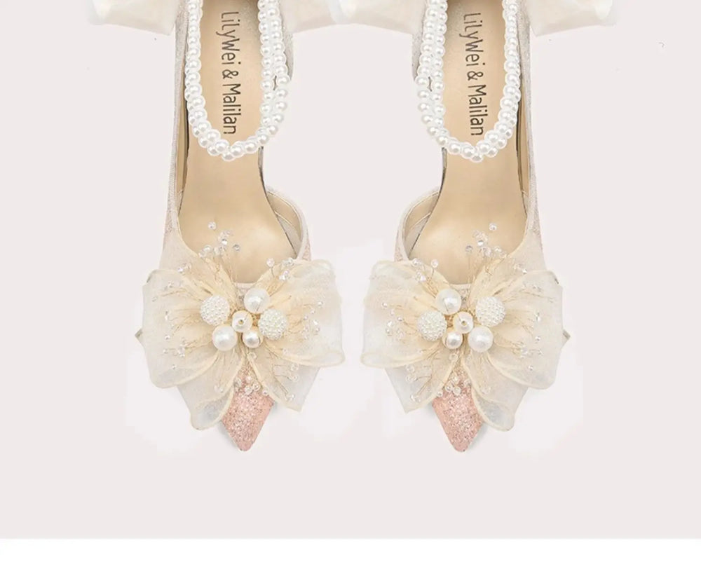 Pair of high-heeled shoes with floral decorations and pearl details on a white background