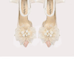 Pair of high-heeled shoes with floral decorations and pearl details on a white background