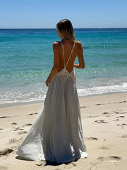 Woman in a white dress standing on a beach with clear blue water and sky.