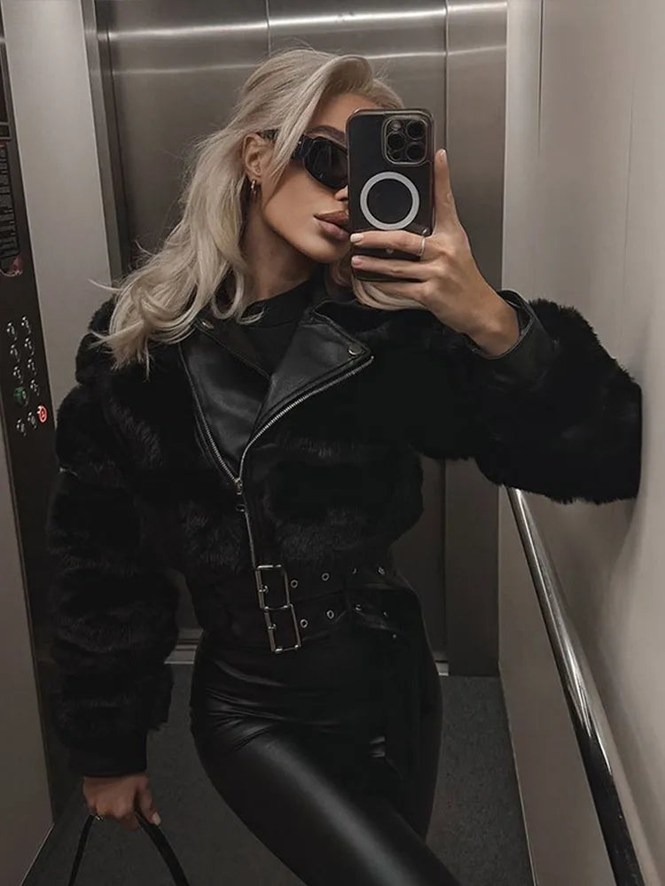 Person taking a mirror selfie wearing a black fur-lined jacket and black pants in an elevator.