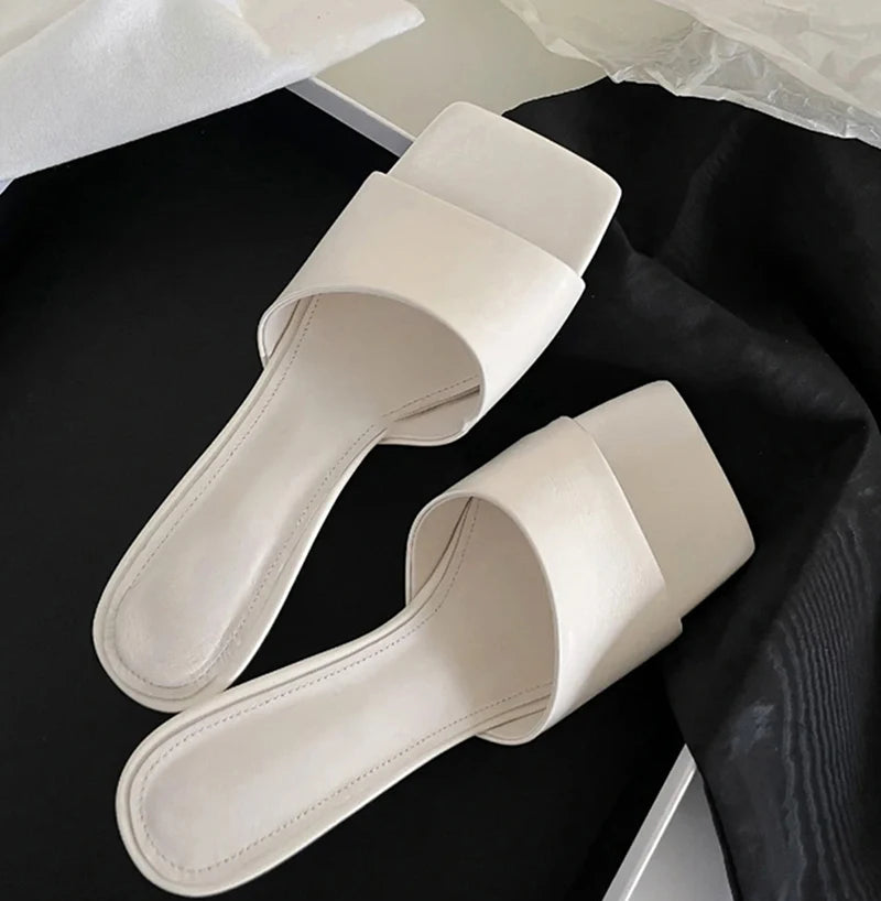 White slide sandals on a black surface with a white background
