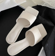 White slide sandals on a black surface with a white background