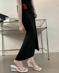 Person wearing a black dress with a red rose detail, standing in an indoor setting.