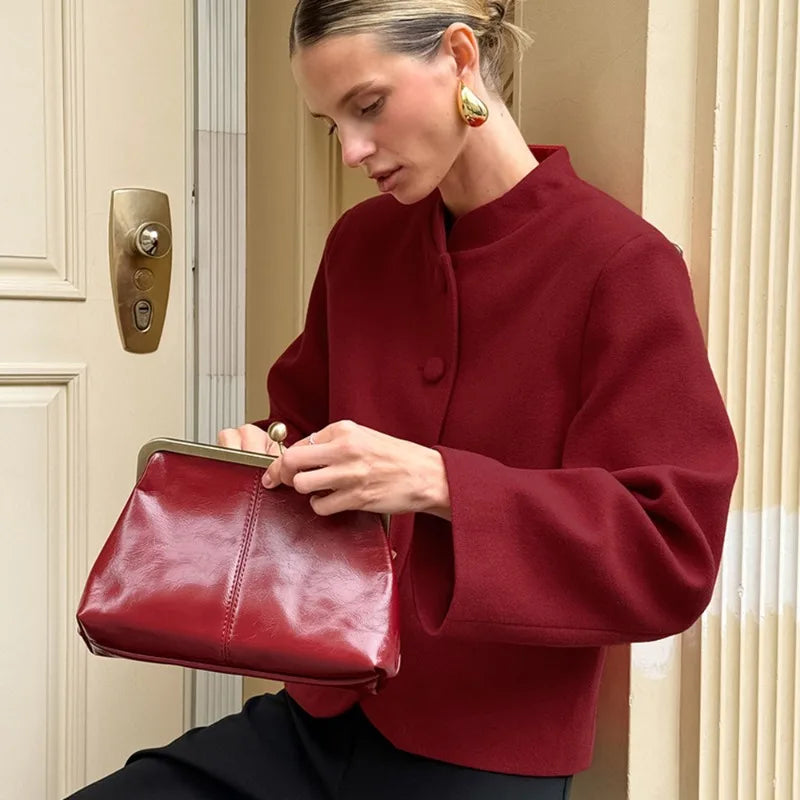 Woman in a red coat holding a red handbag in front of a door.