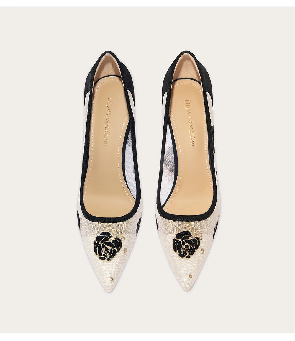 Pair of black and white high-heeled shoes with floral design on a light background