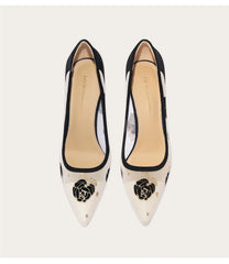 Pair of black and white high-heeled shoes with floral design on a light background