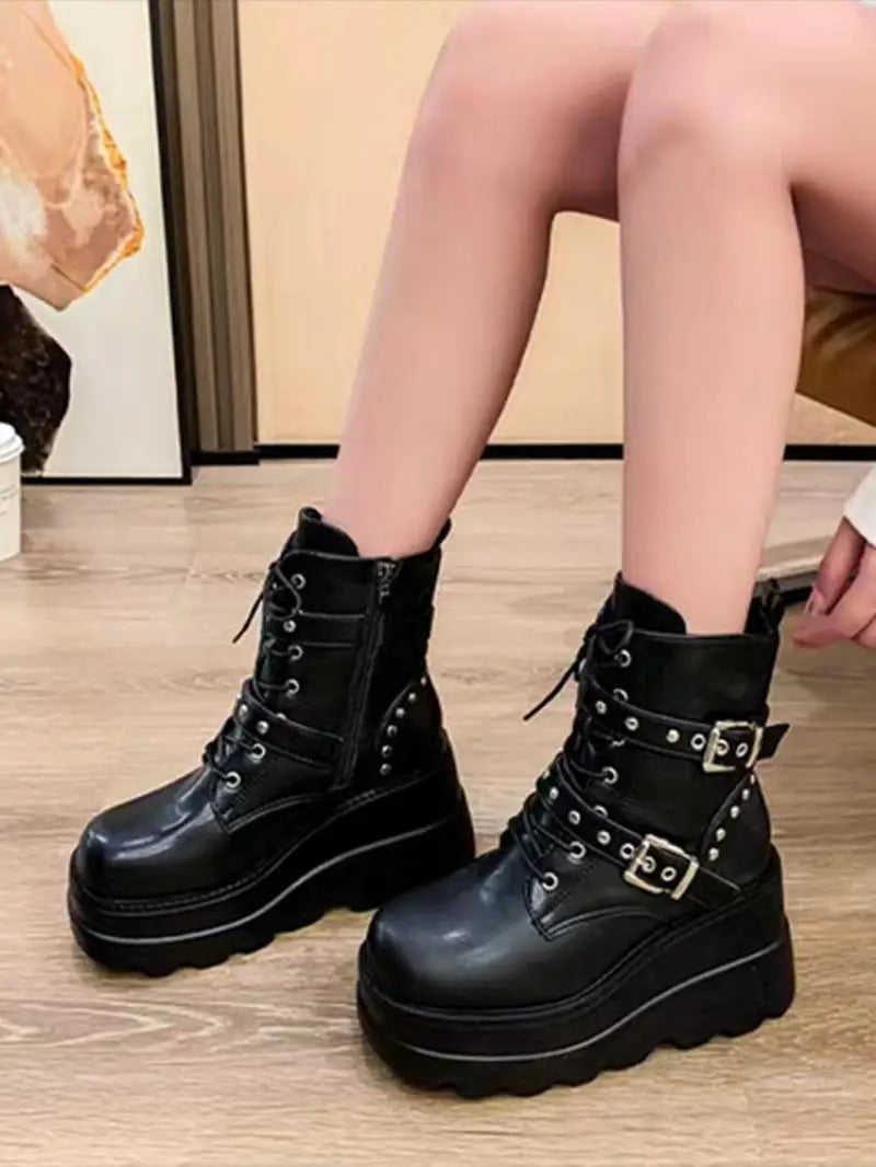 Black platform boots with buckles worn by a person on a wooden floor.