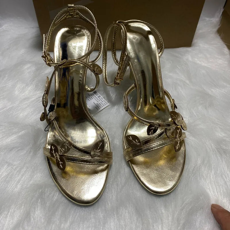 Pair of gold high-heeled sandals on a white fur surface.