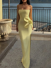 Woman in a strapless yellow evening gown with a large bow standing by a waterfront.