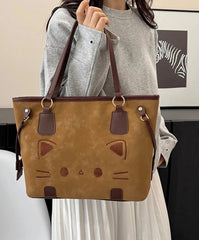 Person holding a brown suede-like tote bag with a cat face design, detail shot