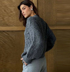 Woman wearing a gray sweater against a wooden paneled wall
