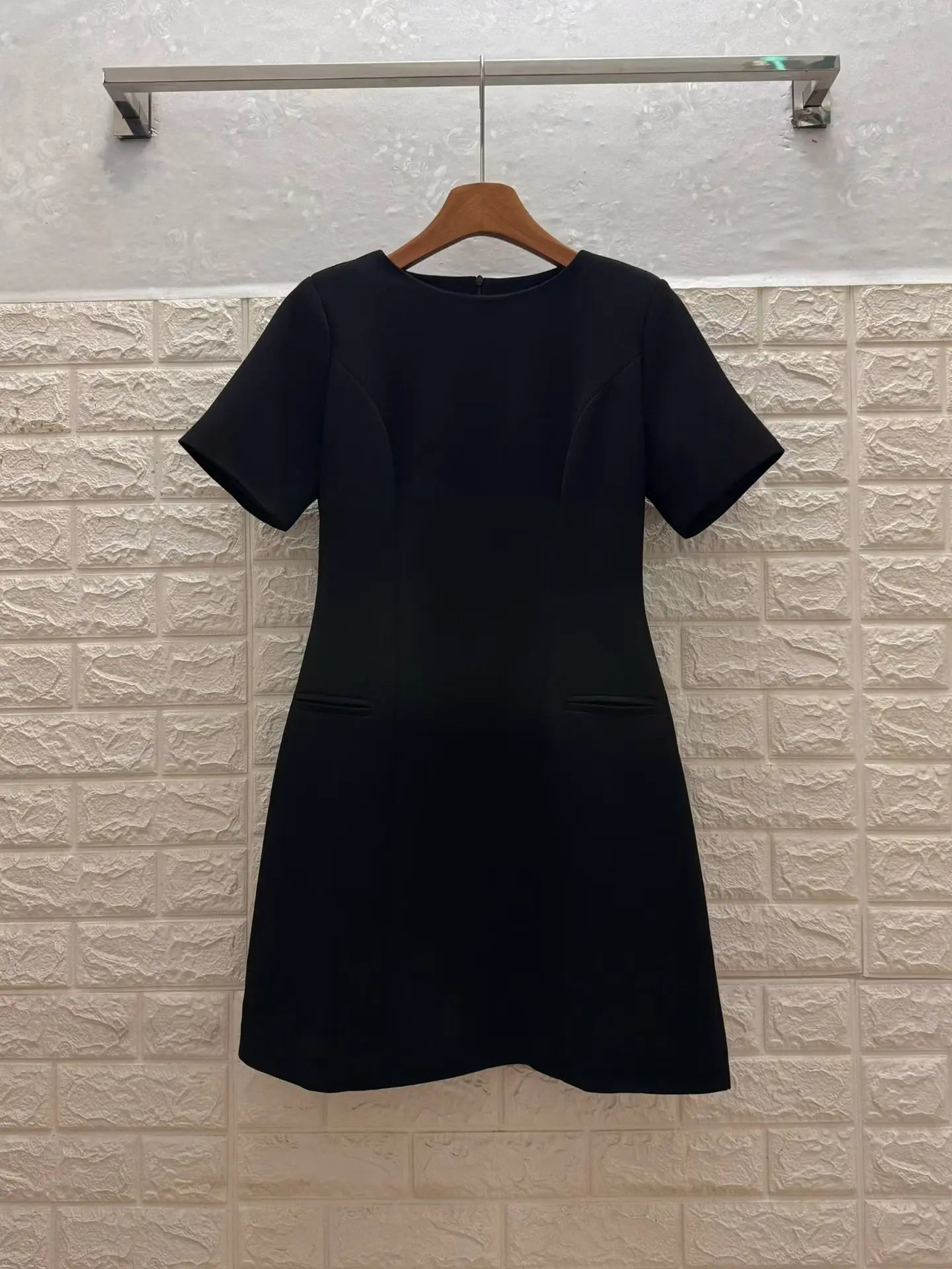 Black dress on a hanger against a textured white wall