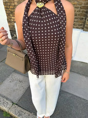 Woman wearing a brown polka dot scarf, white pants, and holding a beige handbag on a street.