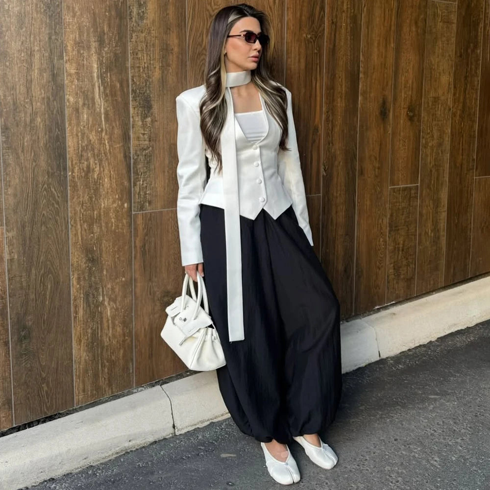 Woman in stylish outfit with white jacket and black pants against a wooden wall.