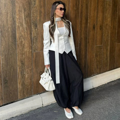 Woman in stylish outfit with white jacket and black pants against a wooden wall.
