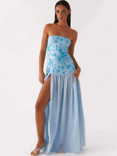 Woman wearing a strapless blue floral dress with a slit on a white background