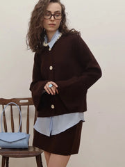 Woman wearing a brown coat over a light blue shirt and skirt, standing.