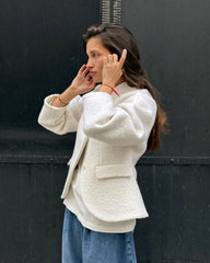 Woman wearing a white textured jacket and blue jeans against a black background