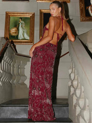 Woman in a burgundy evening gown standing on a staircase with decorative wall art in the background.