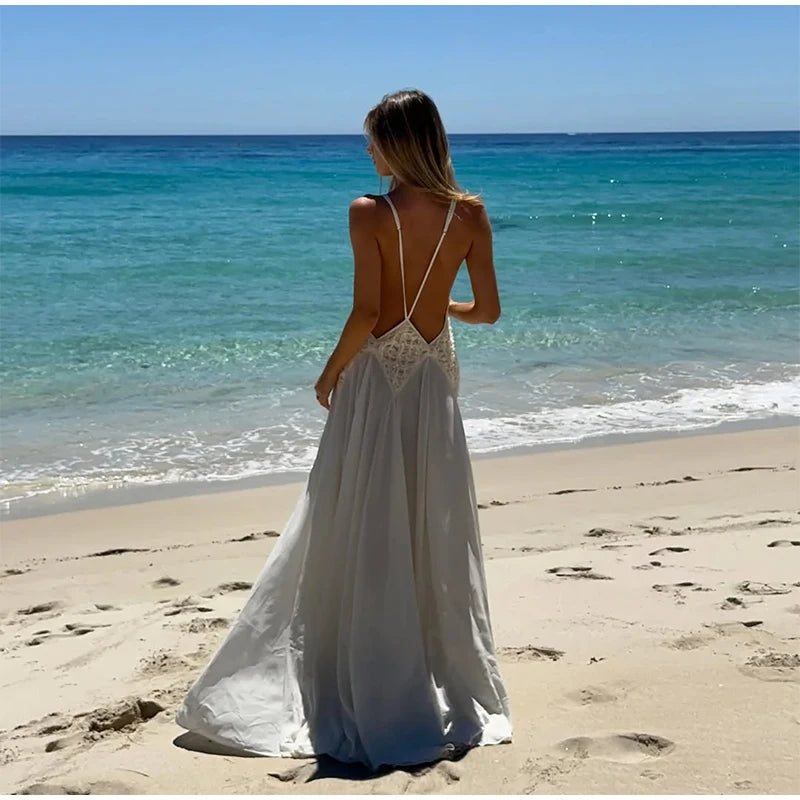 Woman in a white dress standing on a beach with clear blue water and sky.