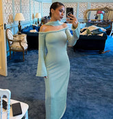 Woman in a light green off-shoulder dress taking a mirror selfie in an ornate room.