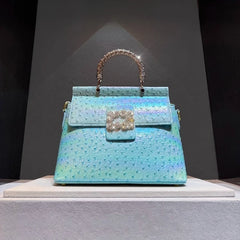 Light blue ostrich embossed top handle bag with crystal clasp and textured handle, displayed on a shelf.