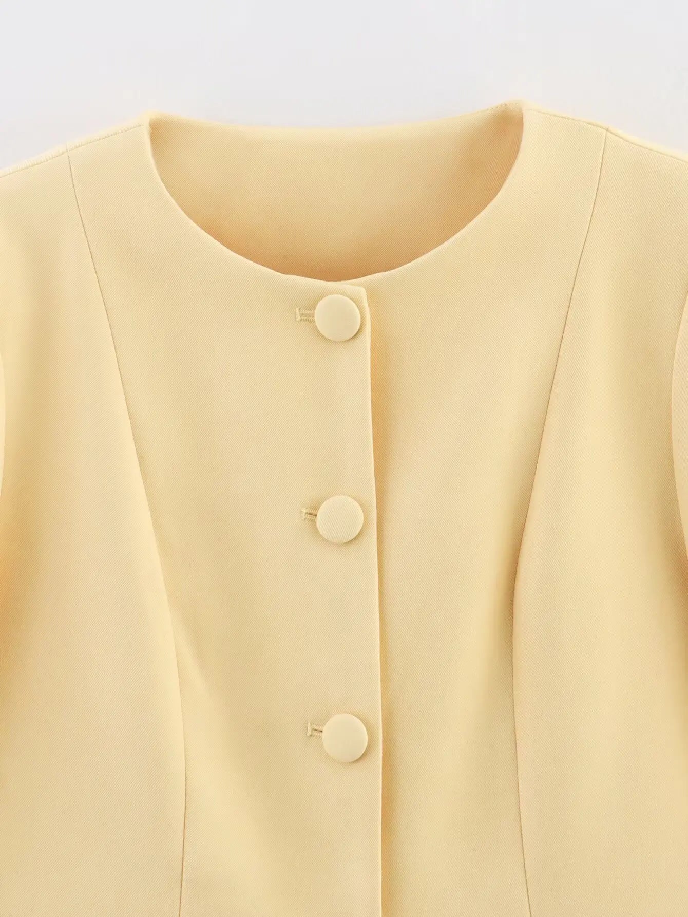 Close-up of a light yellow blouse with buttons on a light gray background