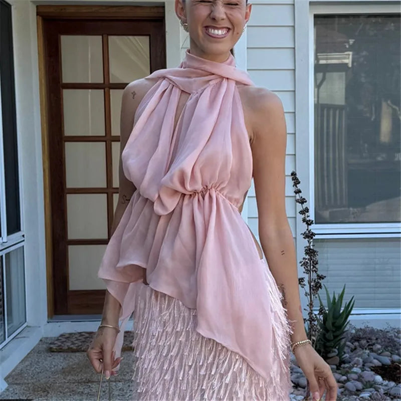 Woman wearing a pink halter top with a matching scarf in front of a house.