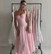 Woman wearing a pink dress standing in front of a rack with other dresses.