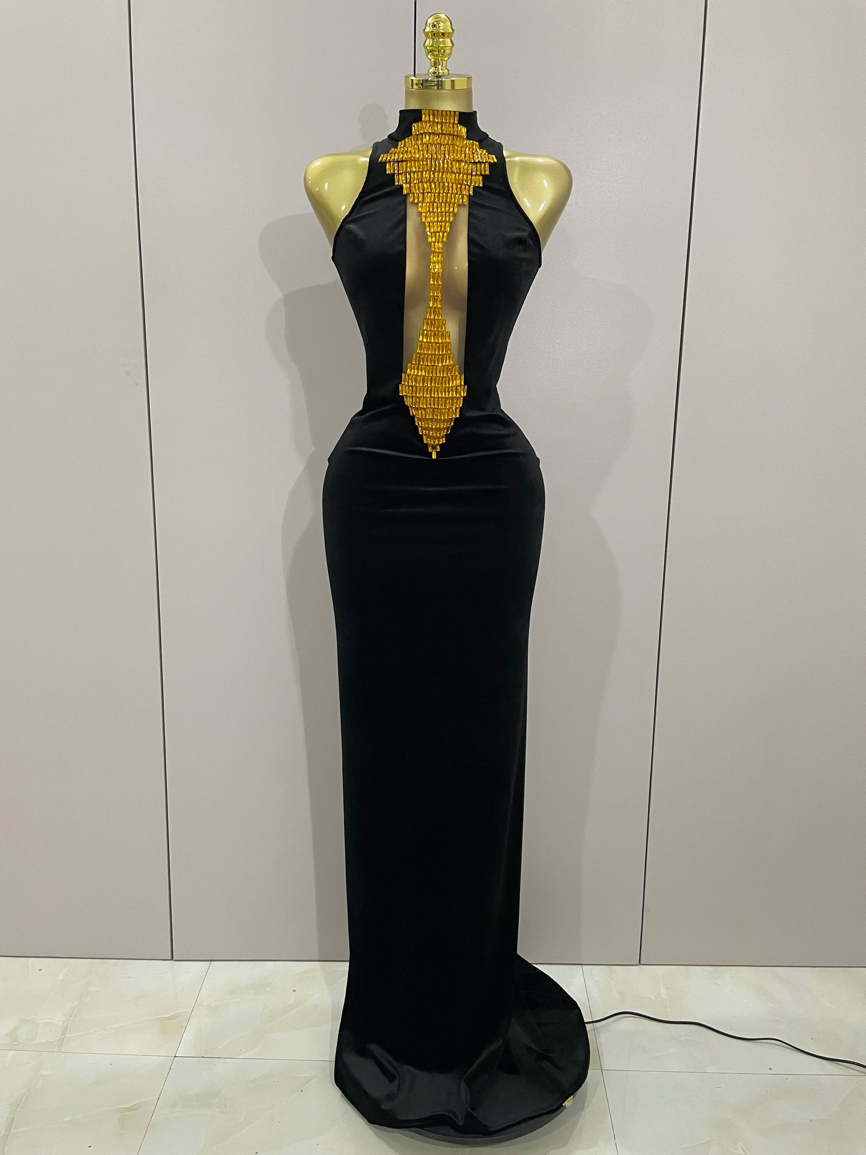 Black evening gown with gold embellishments on a mannequin against a white wall.