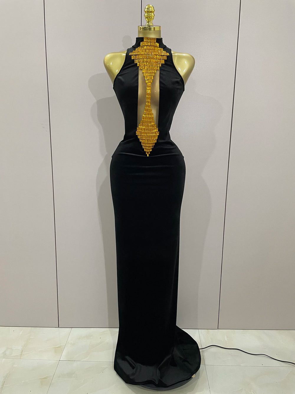 Black evening gown with gold embellishments on a mannequin against a white wall.