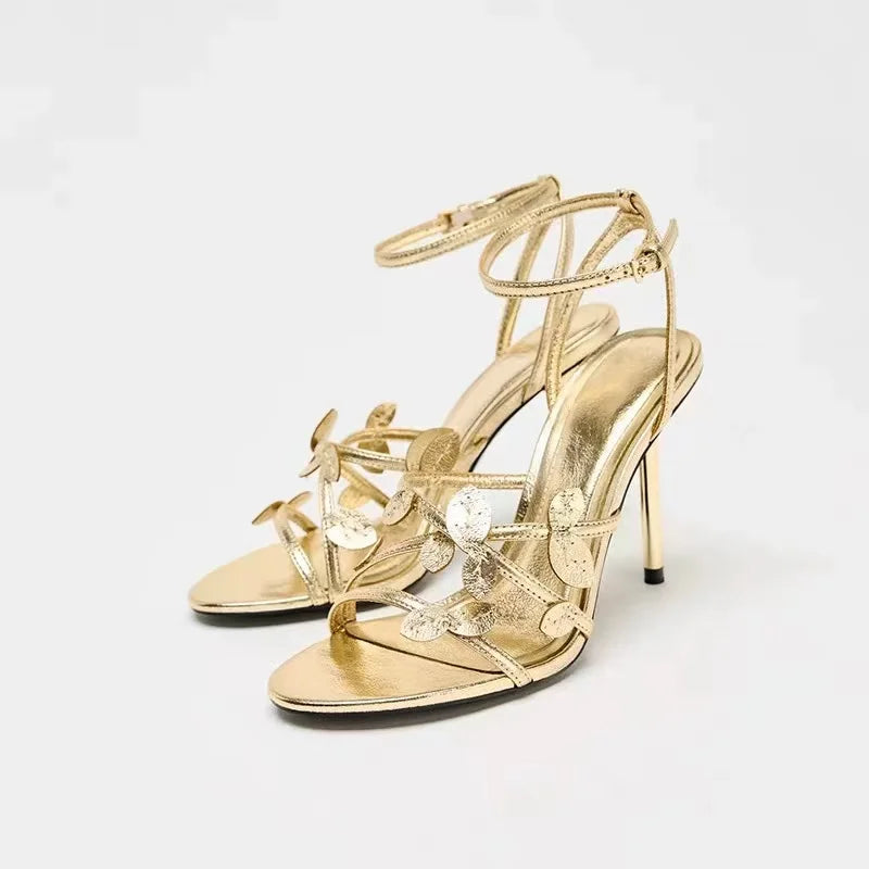 Gold high-heeled sandals with floral details on a white background