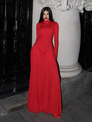 Woman in a red dress standing outdoors next to a decorative column.