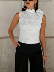Woman wearing a white sleeveless top with a floral detail against a light-colored wall.