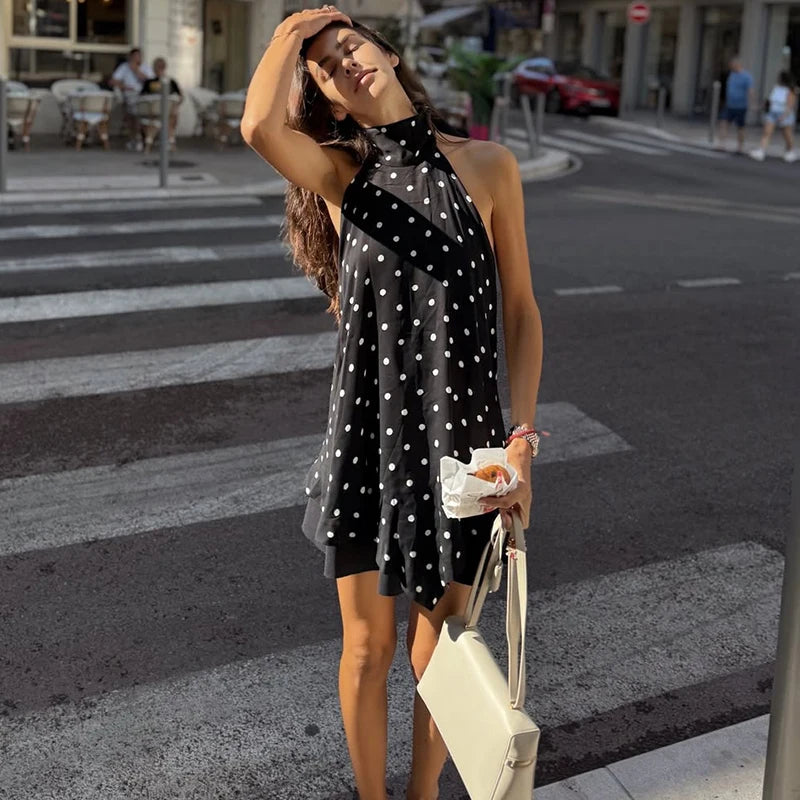 Woman in a black polka dot dress crossing a street with a white handbag.