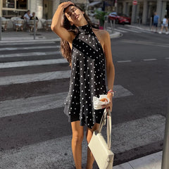 Woman in a black polka dot dress crossing a street with a white handbag.