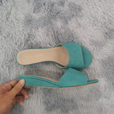Turquoise wedge heel open toe mules on a grey fluffy surface