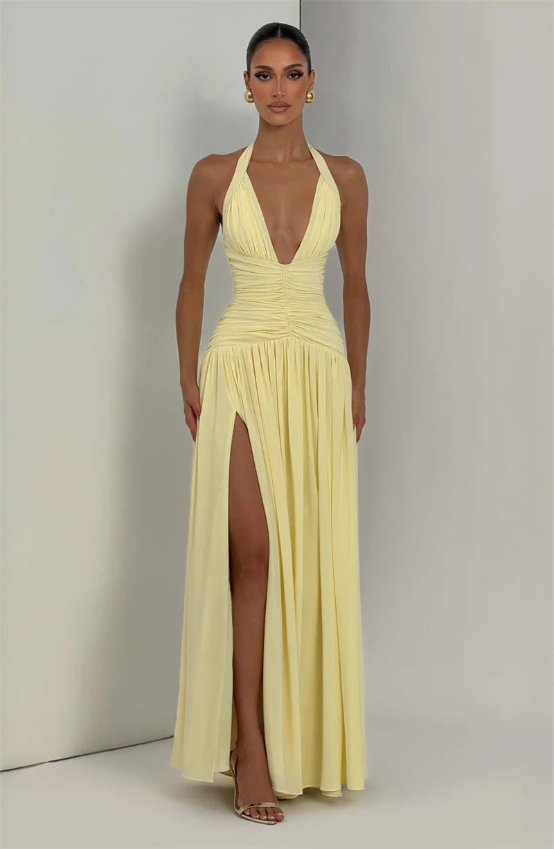 Woman wearing a yellow halter neck gown with a high slit on a plain background
