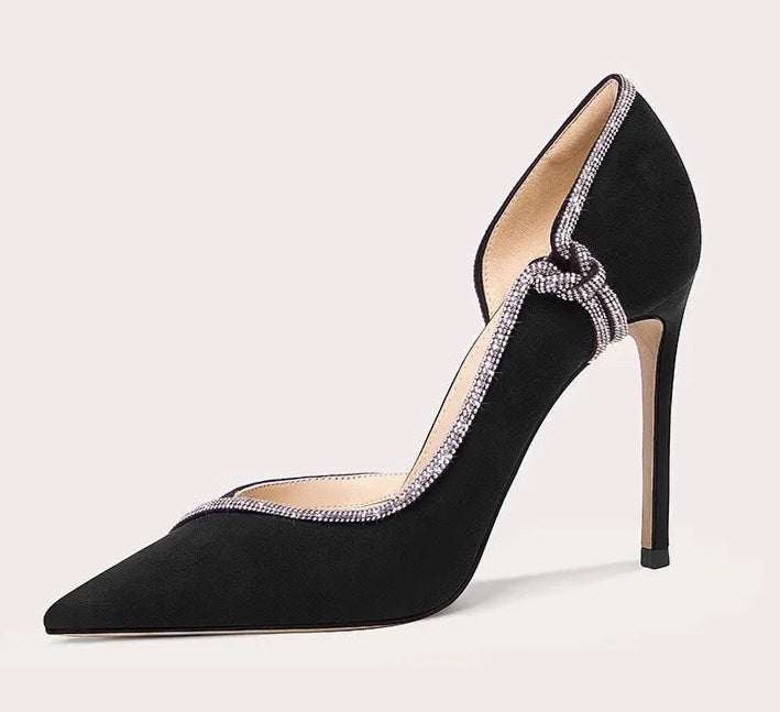 Black high-heeled shoe with decorative strap on a light gray background