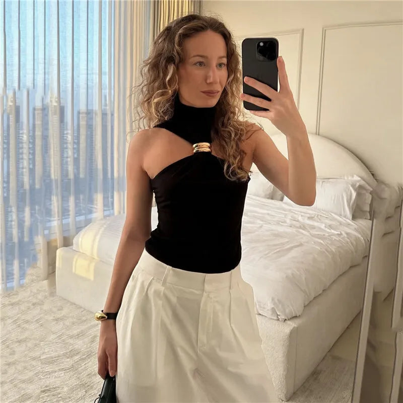 Woman taking a mirror selfie in a stylish black top and white pants in a luxurious room with city view.