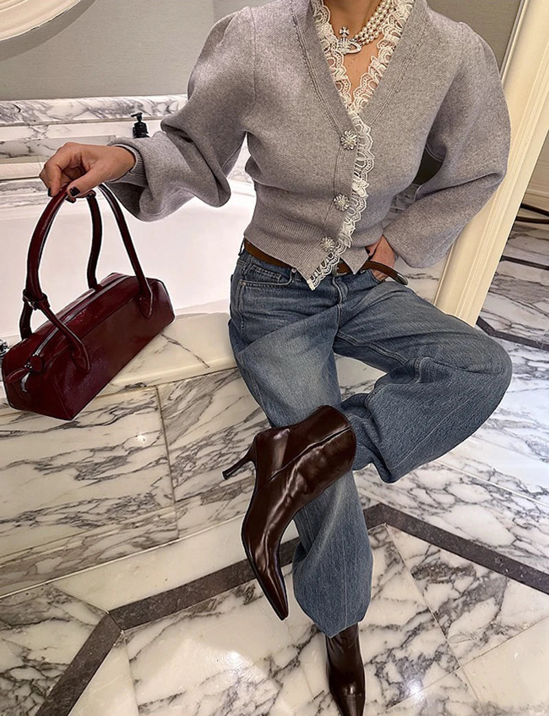 Person wearing a gray cardigan, blue jeans, and brown boots, holding a red handbag on a marble floor.