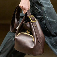 Brown leather handbag with gold hardware held by a person wearing jeans.