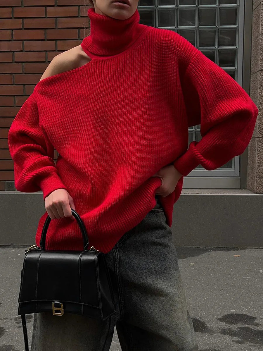 Person wearing a red sweater and holding a black handbag against a brick wall.