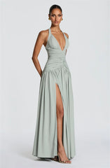 Woman wearing a light green halter neck gown with a high slit on a white background