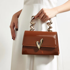 Person holding a brown patent leather evening bag with a sculpted gold heart handle.