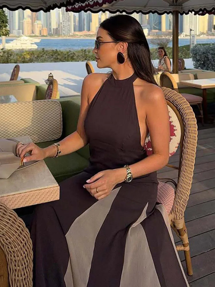 Woman in a brown dress sitting at an outdoor cafe with a cityscape in the background