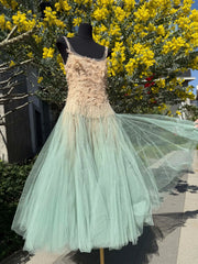 Mannequin wearing a dress with a gradient from beige to green against a yellow flowering bush.