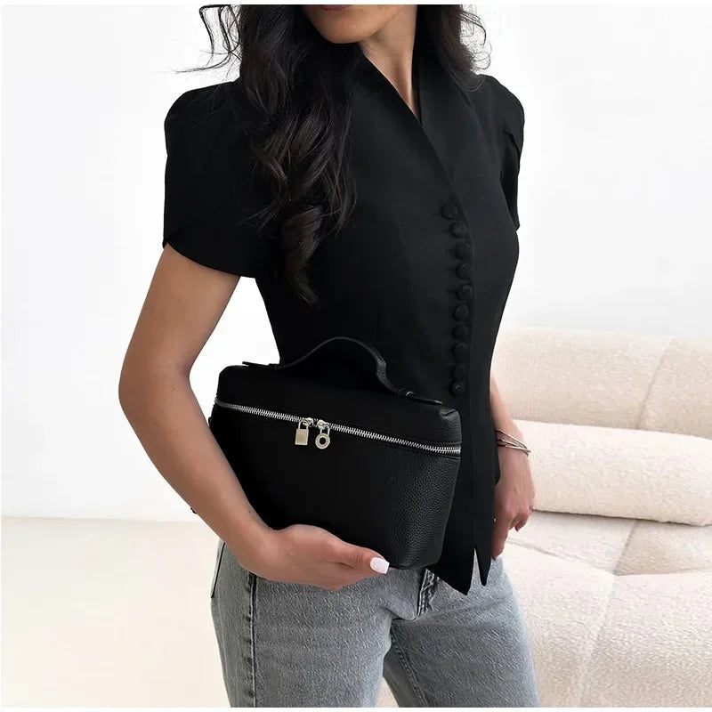 Person holding a black handbag with a neutral background