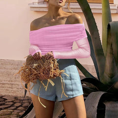 Woman wearing a pink off-shoulder top and blue shorts holding a straw bag outdoors.
